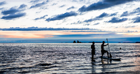 Silhouette of two men surfing board in the waveless sea at dusk.