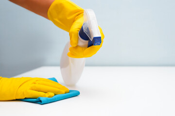 House cleaning, daily routine of hygiene and housework. Side view of woman's hand in rubber yellow glove with rags and cleaning antibacterial spray disinfecting, wiping, polishing surface, indoors