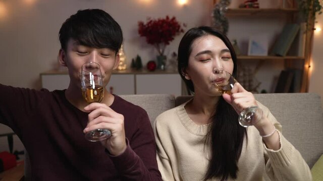 Happy young couple relax sitting on couch in living room on xmas eve. fast movement wife and husband drinking white wine and cheers toasting to camera on video phone call online at home