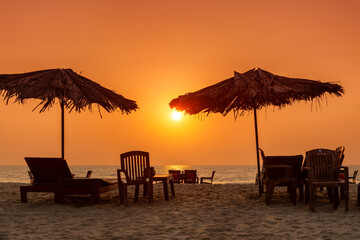 Straw umbrellas with lounge chairs at sunset on a tropical sunny beach in GOA, India