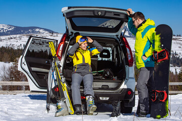 man and woman dressing into ski equipment near suv car