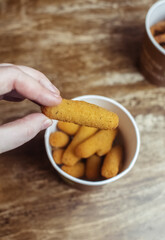 Cheese sticks in a female hand. A large portion of fast food in batter, which lies in a disposable container. Paper bucket for food delivery. Concept of restaurants and fast food cafes
