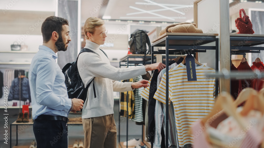 Wall mural handsome male customer shopping in clothing store, retail sales assitant helps with advice. diverse 