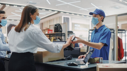 Fototapeta premium Clothing Store Checkout Counter: Retail Sales Managers wearing Protective Face Masks Give Package to Courier for Online Order Delivery. Trendy Designer Brands Available on Internet.
