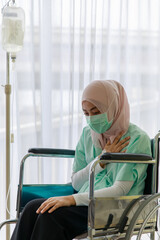 Portrait of ill Muslim wearing patient gown and face mask sitting on a wheelchair with saline fluid bag attach in hospital. Covid 19 pandemic concept