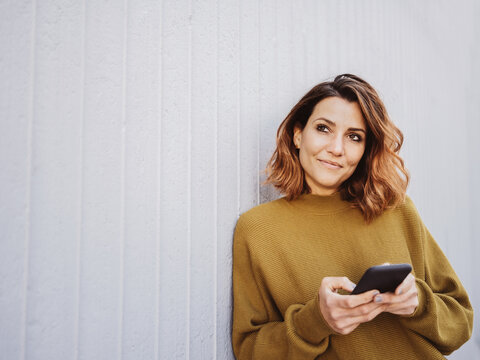Woman holding a mobile phone standing daydreaming