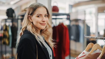 Beautiful Smiling Female Customer Shopping in Clothing Store, Choosing Stylish Clothes, Blouse, Shirt, Looking at Camera. Girl in Fashionable Brands Shop Sustainable Designs. Close-up Portrait