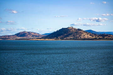 Blue waters of the Hume Dam across Murray River, New South Wales, Australia with sun shining upon hills in background