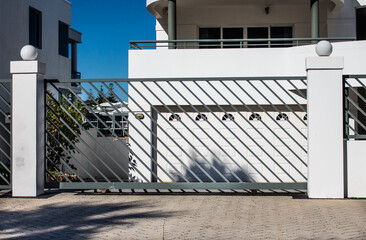Grey modern metal driveway property entrance gates set in concrete fence, lights, trees