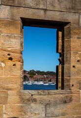 Sandstone brick wall with open window showing boats on water against blue sky