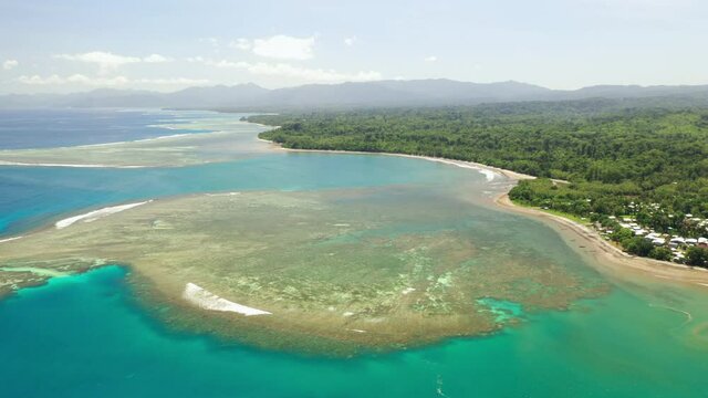 Aerial view of a shallow reef in a harbour and seaside village right up to the mouth of a small creek estuary.