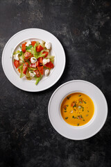 Delicious pumpkin salad and pumpkin puree soup. Healthy food, close-up in a white plate on dark stone. Autumn dishes for Halloween. Flatlay