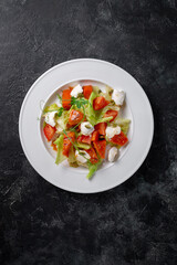 Fresh baked pumpkin salad with tomato, pumpkin seeds, Peking cabbage, feta cheese and vegetable dressing. Healthy food, vegetarian dieting, close up on dark background