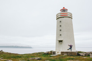 Fototapeta na wymiar tourist in bright pink jacket have fun at the white lighthouse in Iceland