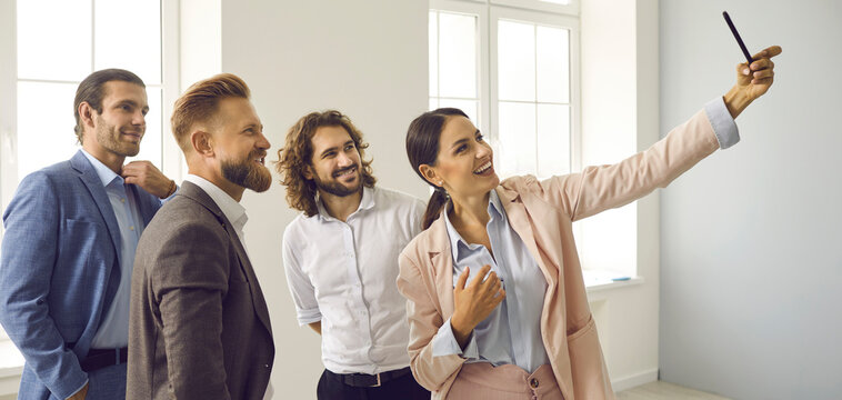 Banner web view of smiling multiracial employees have fun make self-portrait picture on cellphone in office. Happy diverse colleagues laugh take selfie on smartphone at workplace. Technology concept.