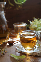 Hot herbal tea with linden flowers and honey on wooden background in sunshine
