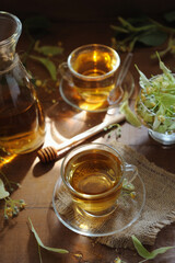Hot herbal tea with linden flowers and honey on wooden background in sunshine