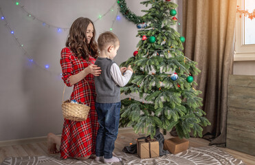 Mom with her child is decorating together the Christmas tree with toys and balls. Concept of family preparation for the New Year, cozy atmosphere and festive mood