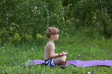 preschooler kid boy meditating during yoga class outside in park in summer time