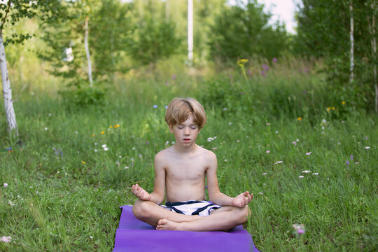 preschooler kid boy meditating during yoga class outside in park in summer time