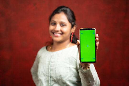 Selective focous on smartphone, Happy smiling Indian girl in traditional dress showing mobile phone with mock up green screen for Diwali festival sale advertisement by looking at camera.