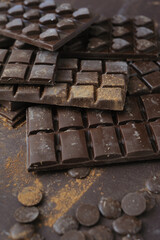 Bars, chopped and chips of dark chocolate on brown background