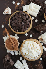 Dark and white chocolate chips, bar, sugar powder, cacao and nutella on brown background