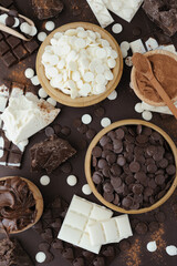 Dark and white chocolate chips, bar, sugar powder, cacao and nutella on brown background