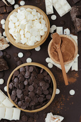 Dark and white chocolate chips, bar, sugar powder, cacao and nutella on brown background