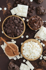 Dark and white chocolate chips, bar, sugar powder, cacao and nutella on brown background