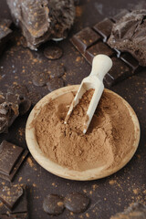 Cacao powder in wooden bowl with chopped and chips of  dark chocolate