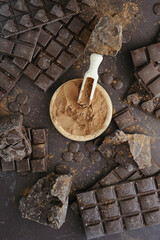 Bars, chopped and chips of  dark chocolate with cacao powder in wooden bowl