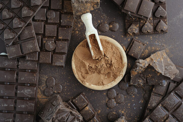 Bars, chopped and chips of  dark chocolate with cacao powder in wooden bowl