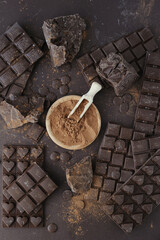 Bars, chopped and chips of  dark chocolate with cacao powder in wooden bowl