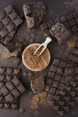 Bars, chopped and chips of  dark chocolate with cacao powder in wooden bowl