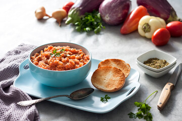 Eggplant caviar in blue bowl and fresh vegetables on background
