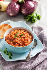 Eggplant caviar in blue bowl and fresh vegetables on background