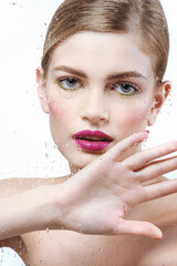 Beautiful young woman in water splash behind the glass with water drops