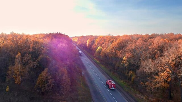 View of the highway located in a beautiful wooded area. The sun's rays illuminate the yellow crowns of trees. Truck and fire truck moving in different directions. High quality. 4k footage.