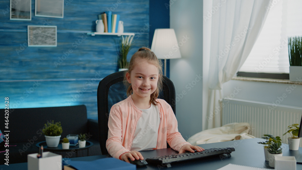 Poster portrait of child sitting at desk with computer for online lessons at home. elementary school girl u