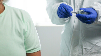 Doctor in blue latex gloves fill in syringe with medicine from glass vial for injection of an elderly person in medical laboratory against coronavirus, flu, measles disease