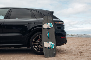 Close-up surfboard and kite equipment on sand beach near-luxury SUV car