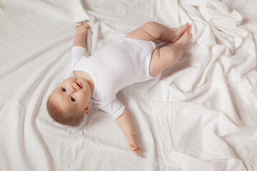 charming newborn baby in a white bodysuit lies on his back on a white fabric. top view. products...