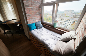 View of cozy windowsill bed in loggia. Design of modern appartment with sleeping place on windowsill and wooden flooring. Concept of loft style.