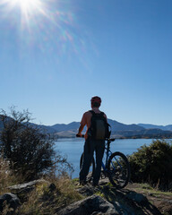 Obraz premium Tourist riding the bike on Glendhu Bay track along Lake Wanaka with mountains in the distance, South Island. Vertical format.