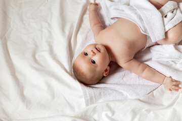 cute newborn baby wrapped in a white towel lies on a bed with white cotton underwear. cleanliness, hygiene. products for children. concept of happy childhood and motherhood. child care. space for text