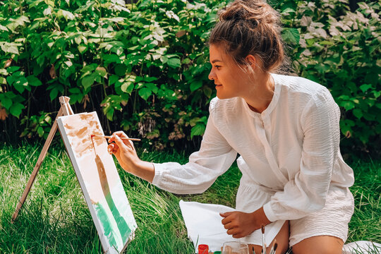 Woman Painting On Canvas While Sitting At Backyard