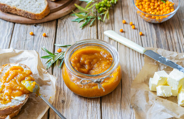 Sea buckthorn jam in a glass jar and spread on the bread with butter, fresh berries and leaves 