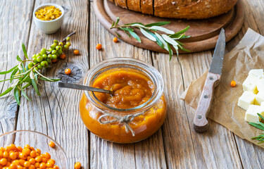 Sea buckthorn jam in a glass jar with butter, fresh berries, leaves and loaf bread