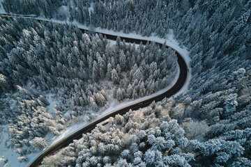 Aerial view of winter landscape with snow covered mountain hills and winding forest road in morning.